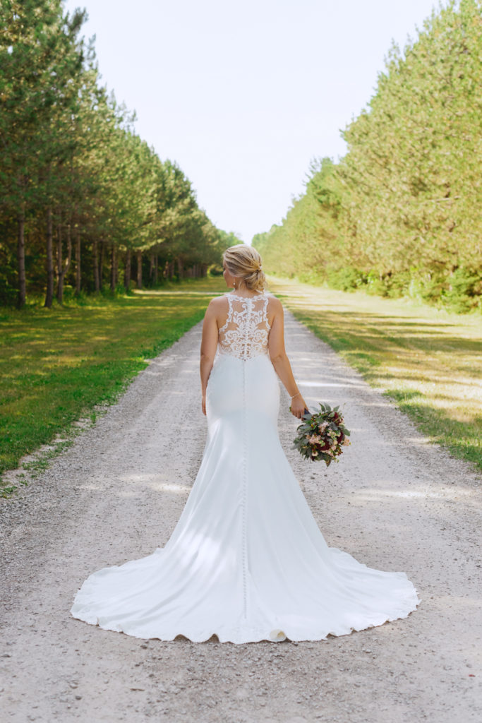 bride's beautiful lace back dress from behind standing on dirt road