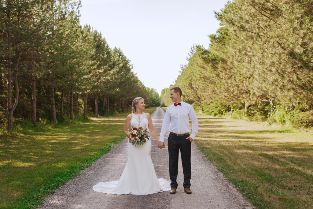 bride and groom holding hands on a dirt road smiling at each other