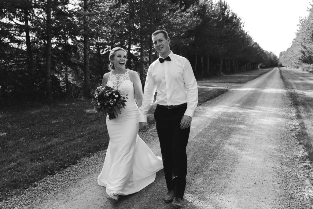 bride and groom walking down dirt road laughing