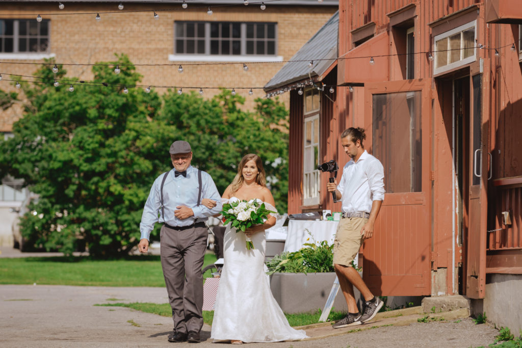 bride and her father making their way out red barn to walk down the aisle