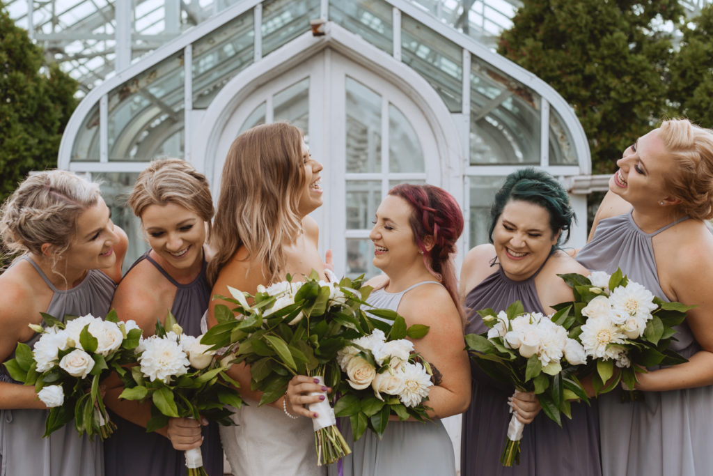 bridesmaids laughing in front of greenhouse at the experimental farm