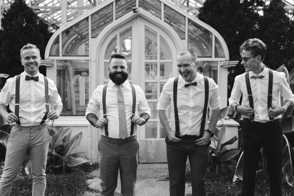 groom and groomsmen laughing in front of greenhouses