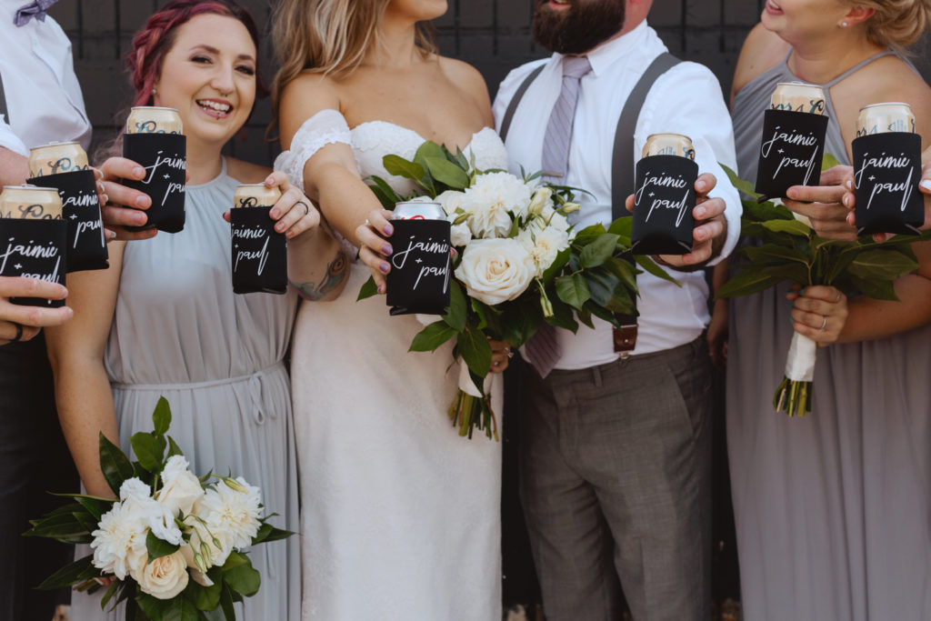 wedding party holding beers with cozy that says bride and groom's name
