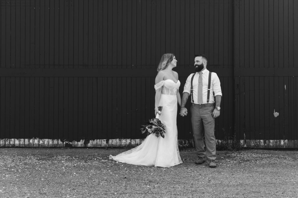black and white photo of bride and groom holding hands in front of a big black barn door