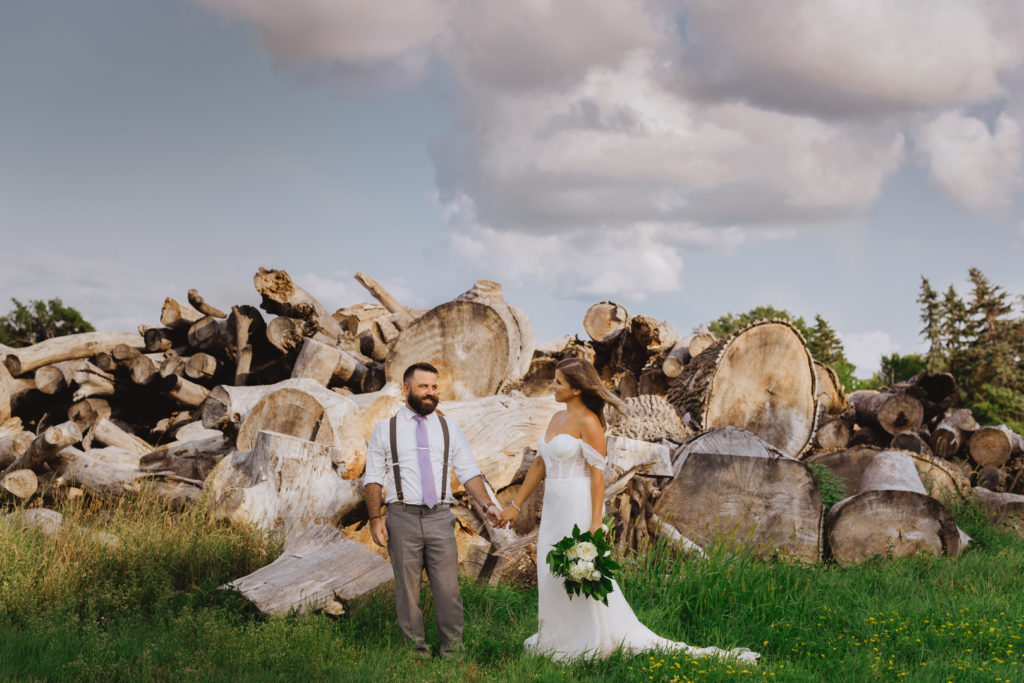bride and groom holding hands in field with a pile of logs