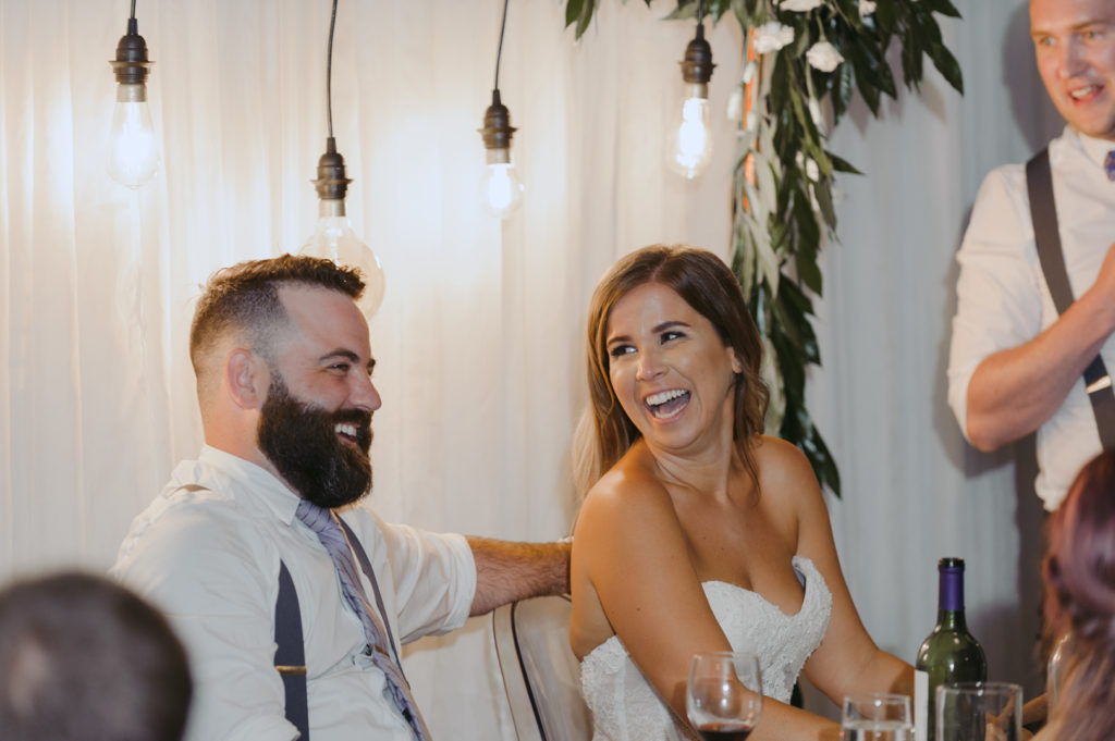 bride and groom laughing at speech during wedding reception
