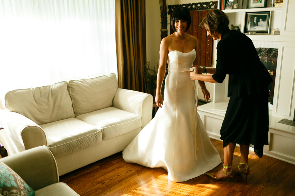 mother of the bride helping the bride into her wedding dress