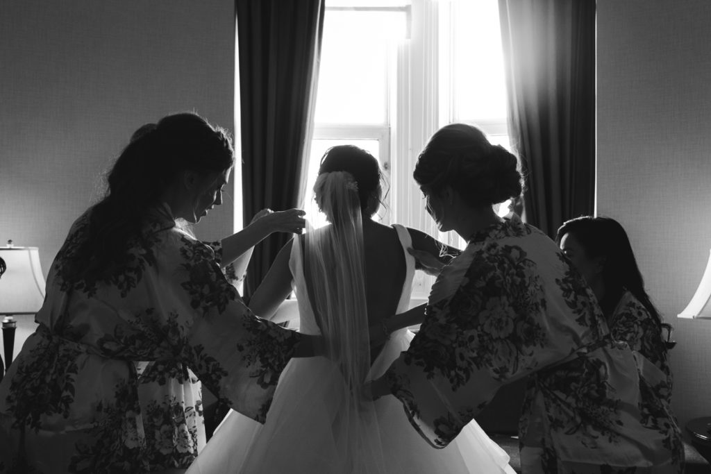 bridesmaids helping the bride into her dress