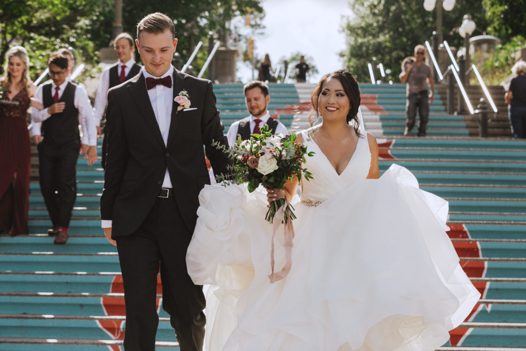 groom helping bride with her train as they walk down stairs