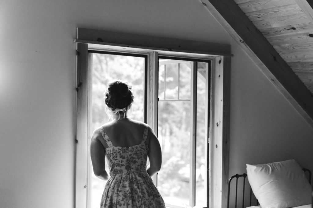 bride gazing out the window as guests start to arrive to wedding