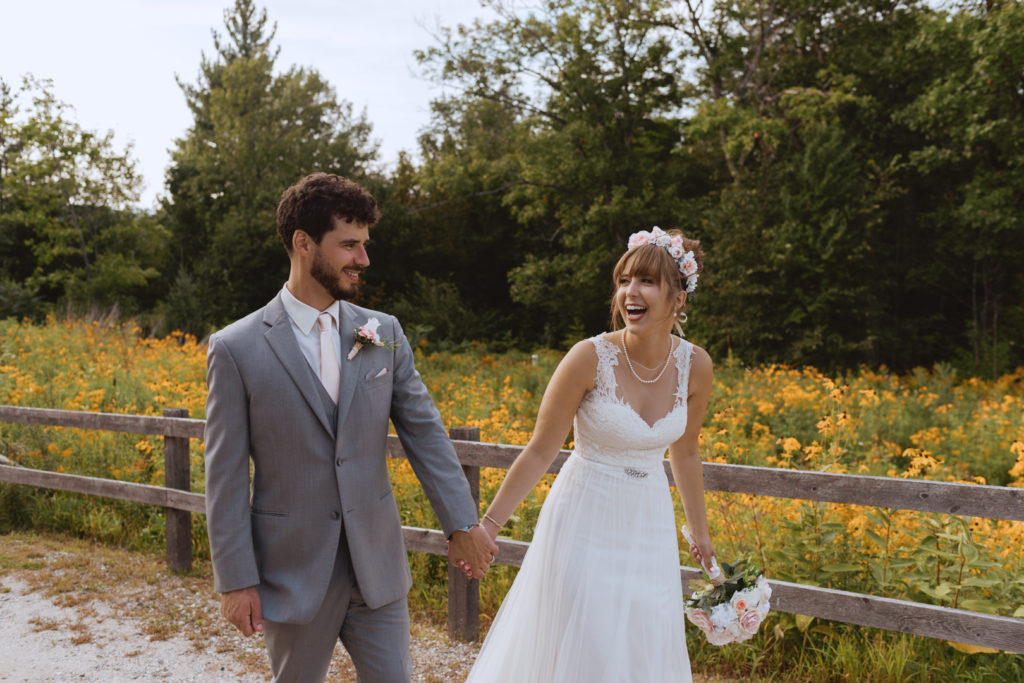 bride and groom holding hands walking throw field of yellow daisies