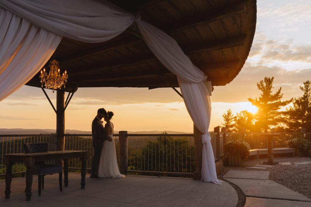 bride and groom standing under gazebo on a cliff at sunset