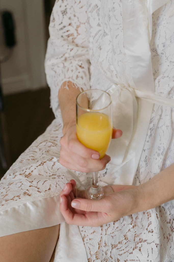 bride holding a mimosa while getting her makeup done