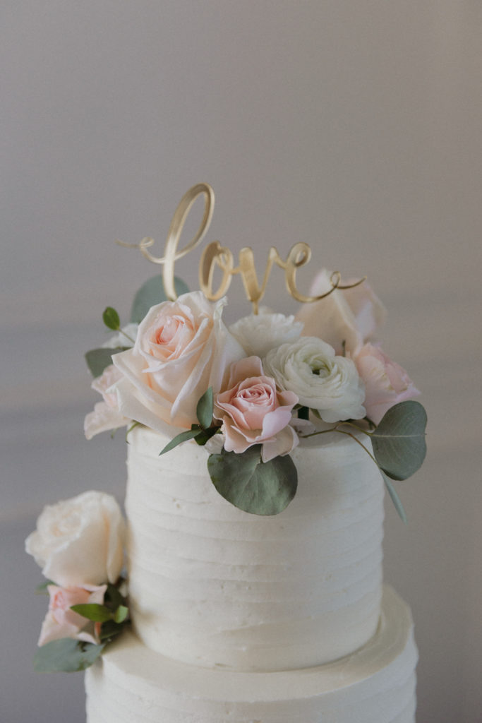 wedding cake with blush flowers and 'love' cake topper