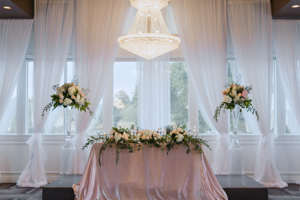 blush and green head table underneath crystal chandelier