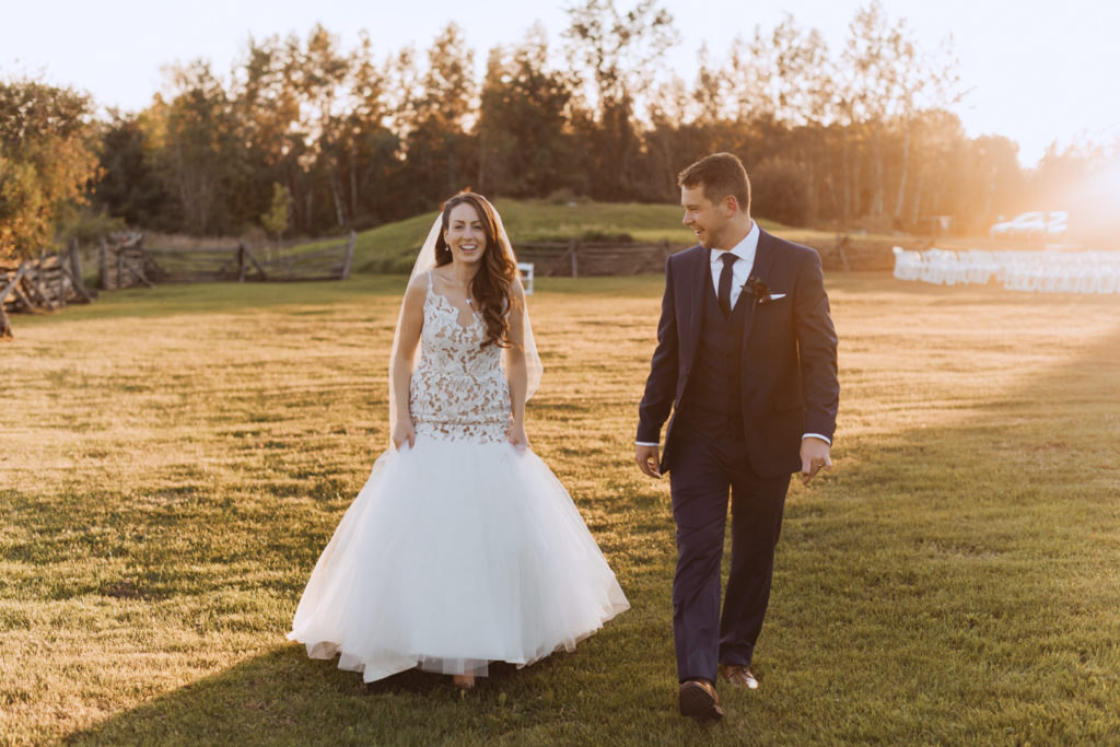 bride and groom walking into field at sunset laughing