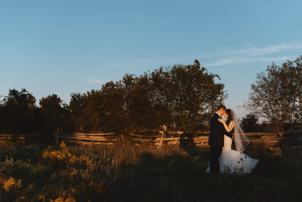 bride and groom cuddling in field at sunset
