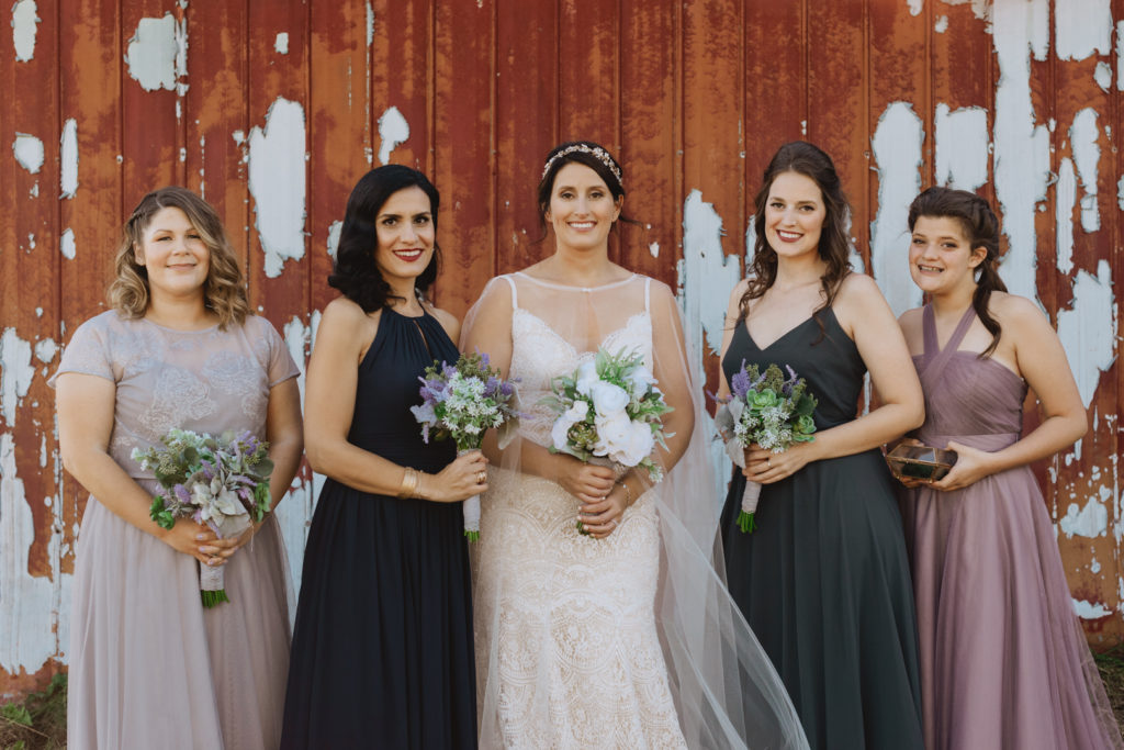 bride and bridesmaids standing in front of old red barn