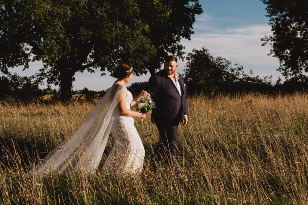 bride and groom walking through field at sunset