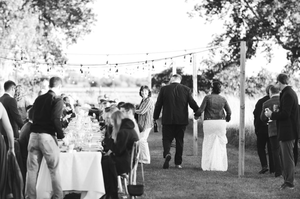 bride and groom walking down long harvest table to wedding reception