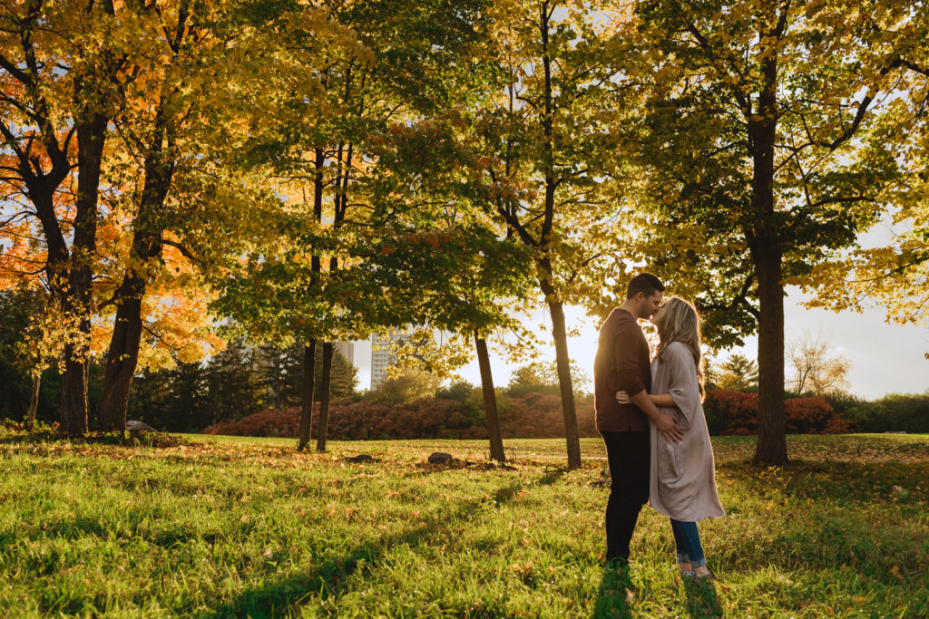 engaged couple kissing at sunset among the trees