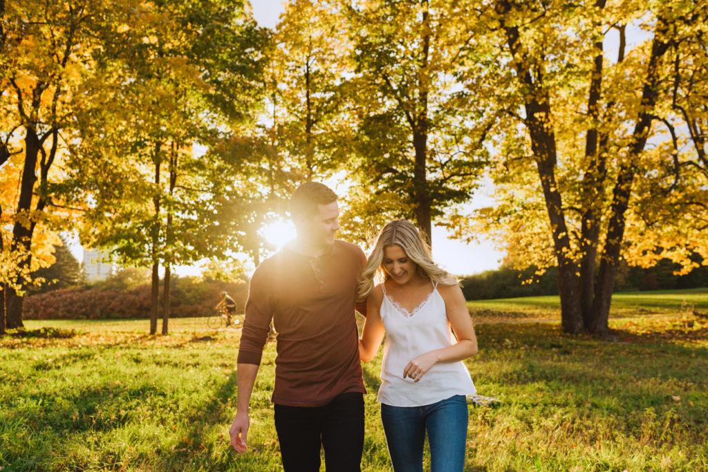 engaged couple walking together laughing at sunset in a field with trees