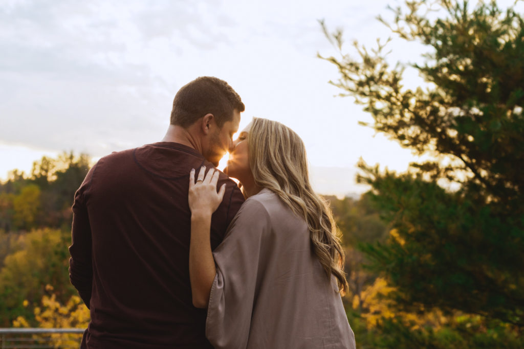 engaged couple kissing as sun sets behind them