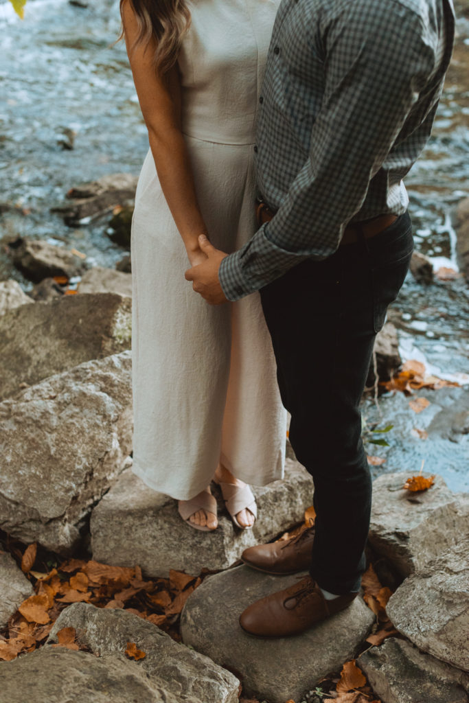 engaged couple standing on rocks holding hands