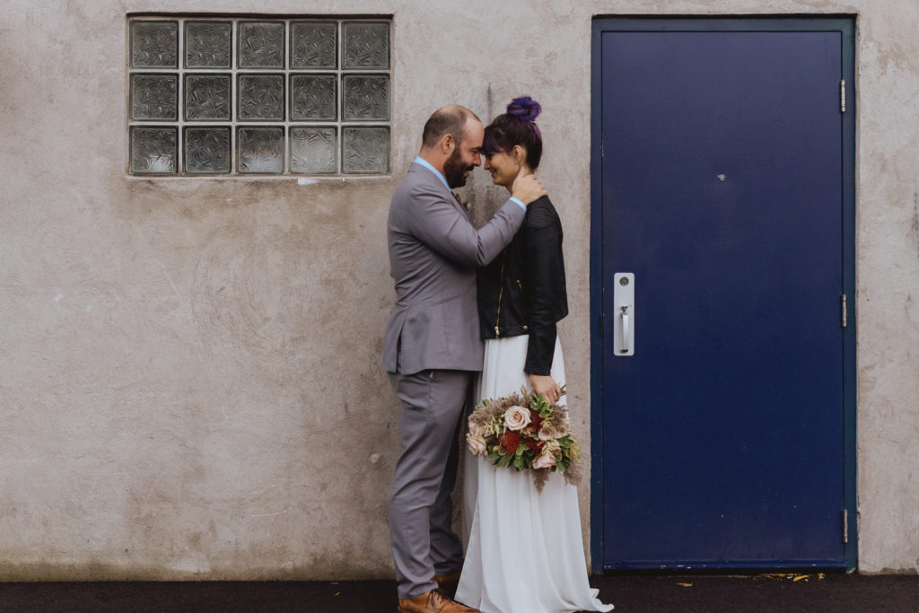 bride and groom cuddling next to purple door