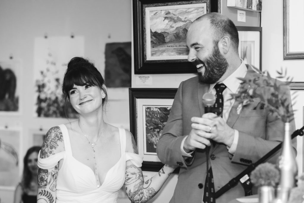 bride smiling while groom gives a toast