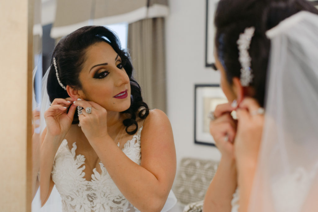bride putting on her earrings in the mirror