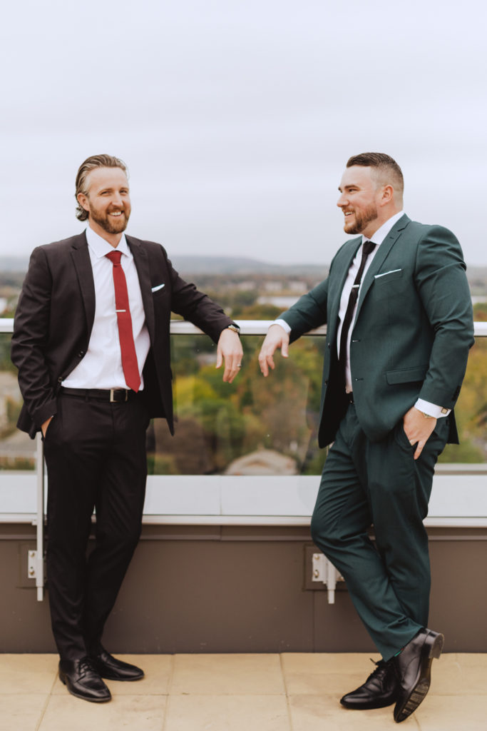 groom and best man laughing on rooftop balcony