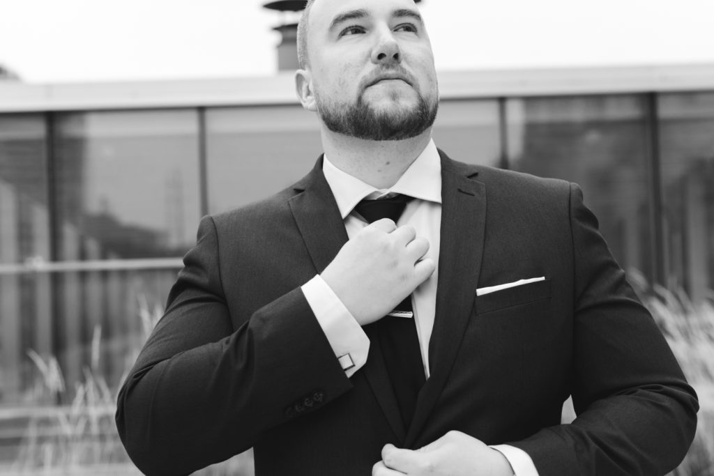 groom adjusting his tie in black and white