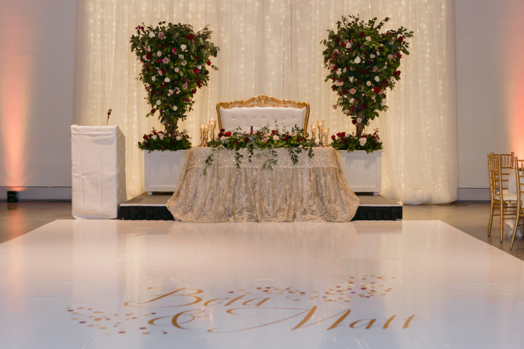 sweetheart table with large floral arrangement and decal on the dance floor with bride and groom's name