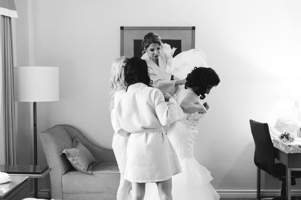 mother of the bride and bridesmaids helping the bride into her wedding dress