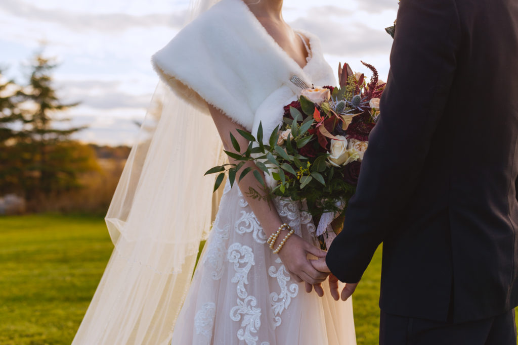 bride and groom holding hands and wedding bouquet at sunset