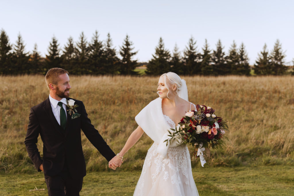 bride and groom holding hands walking in a field at sunset