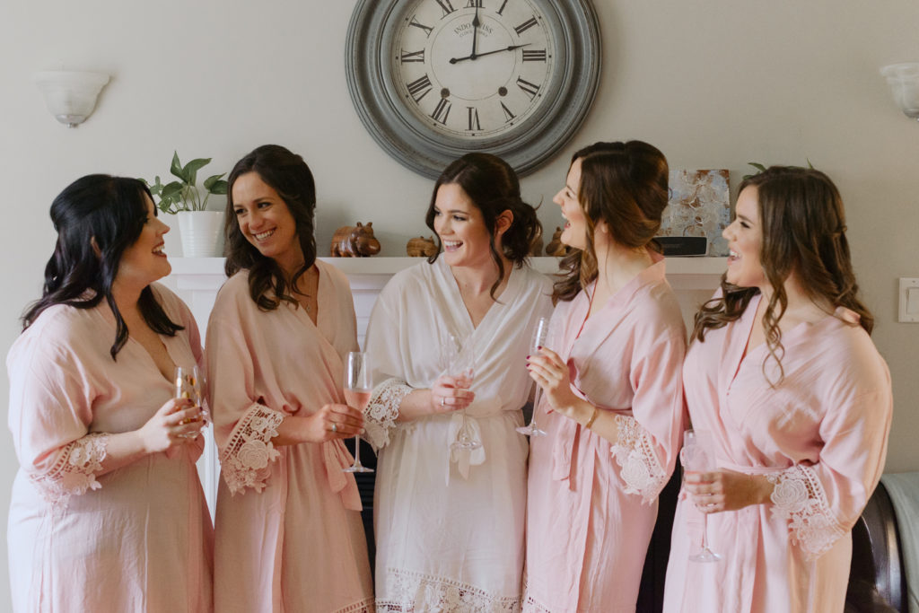bride and bridesmaids with champagne laughing in lace robes