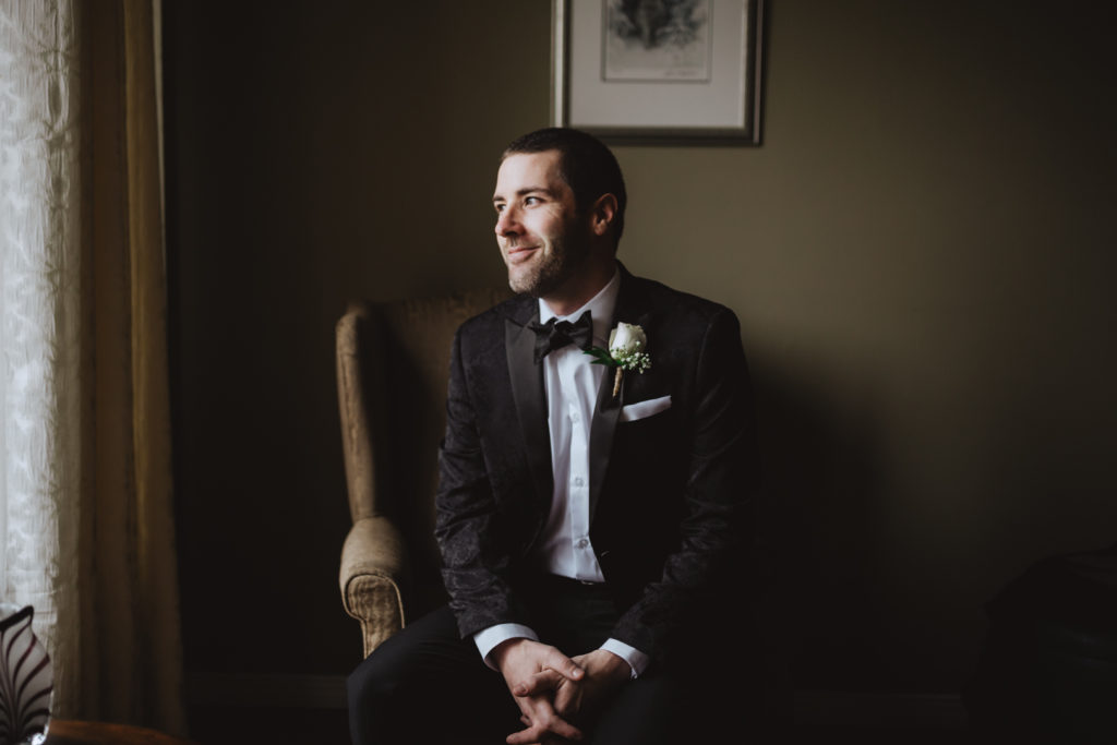groom sitting in a chair by the window smiling