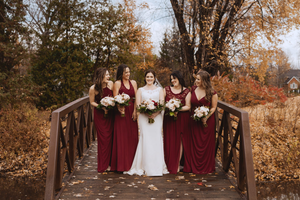 bride and bridesmaids on a wooden bridge surrounded by fall leaves