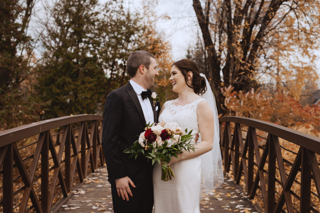 bride and groom on wooden bridge surrounded by fall leaves