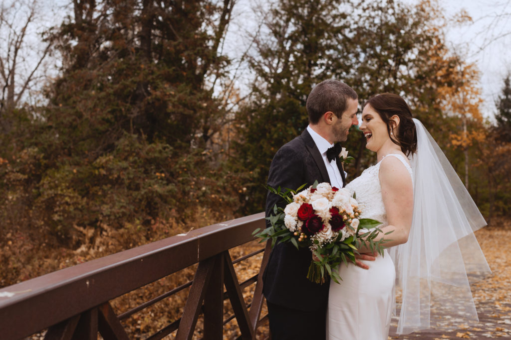 bride and groom on wooden bridge surrounded by fall leaves