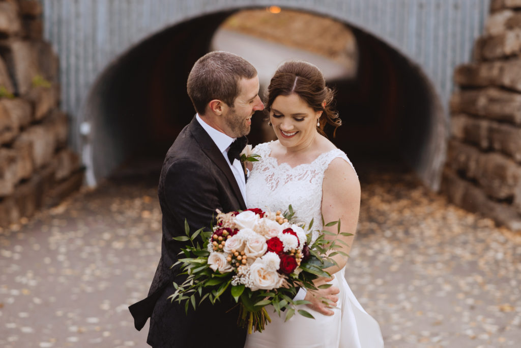 bride and groom standing in front of metal tunnel laughing