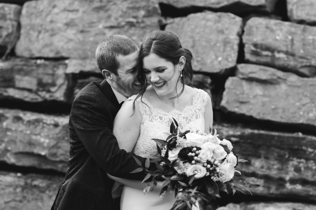 bride and groom cuddling and laughing in front of large rock wall