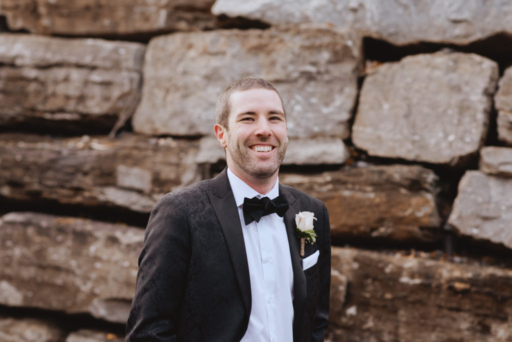 groom in a tux smiling in front of a large rock wall