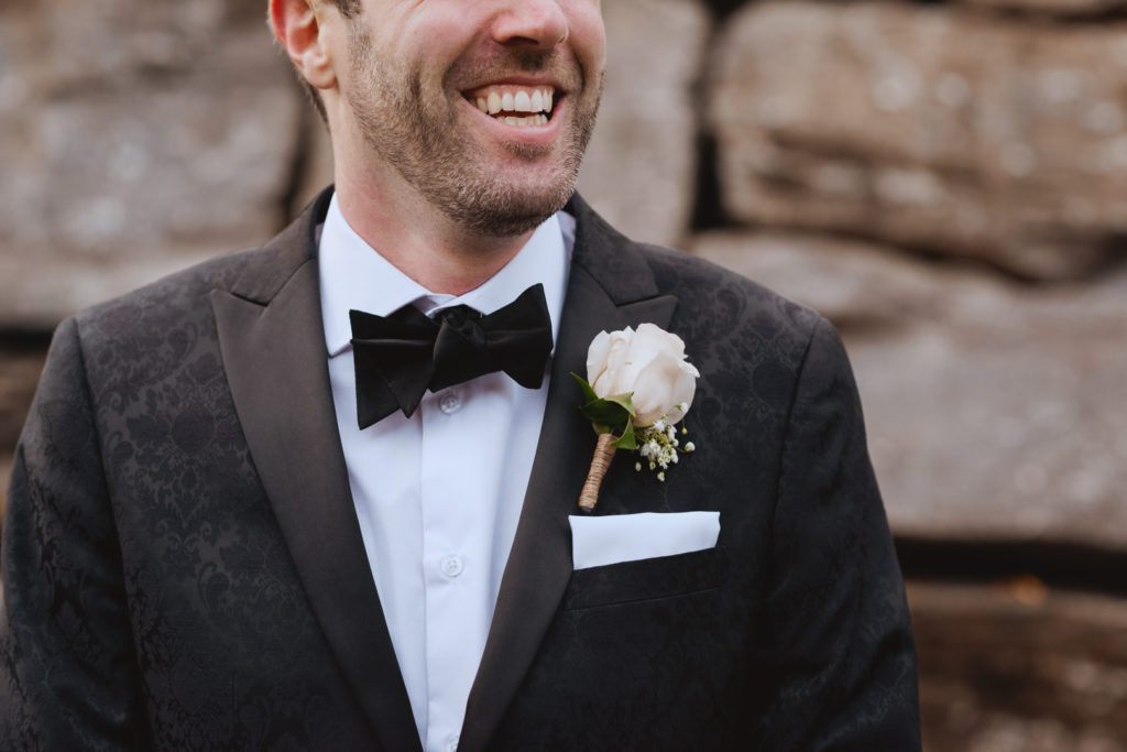 groom laughing in front of large rock wall