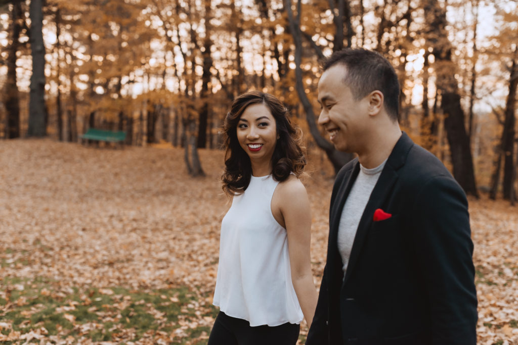 engaged couple walking in a field of autumn leaves laughing