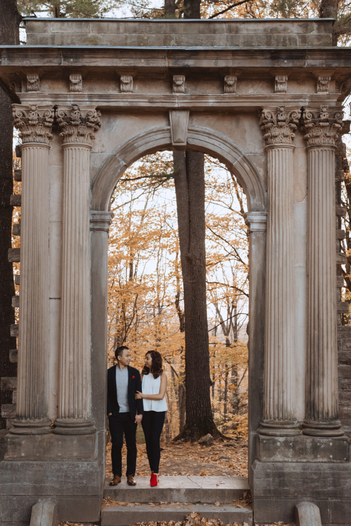 engaged couple holding hands underneath stone arch at Mackenzie King Estate