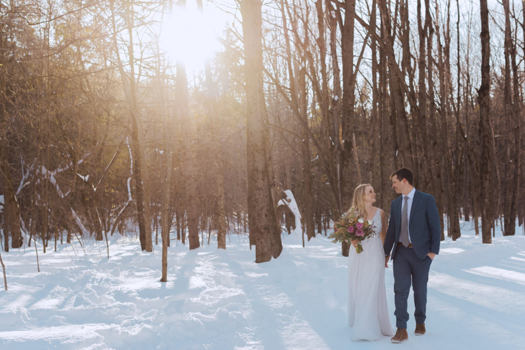 bride and groom walking through the forest in the winter at sunset