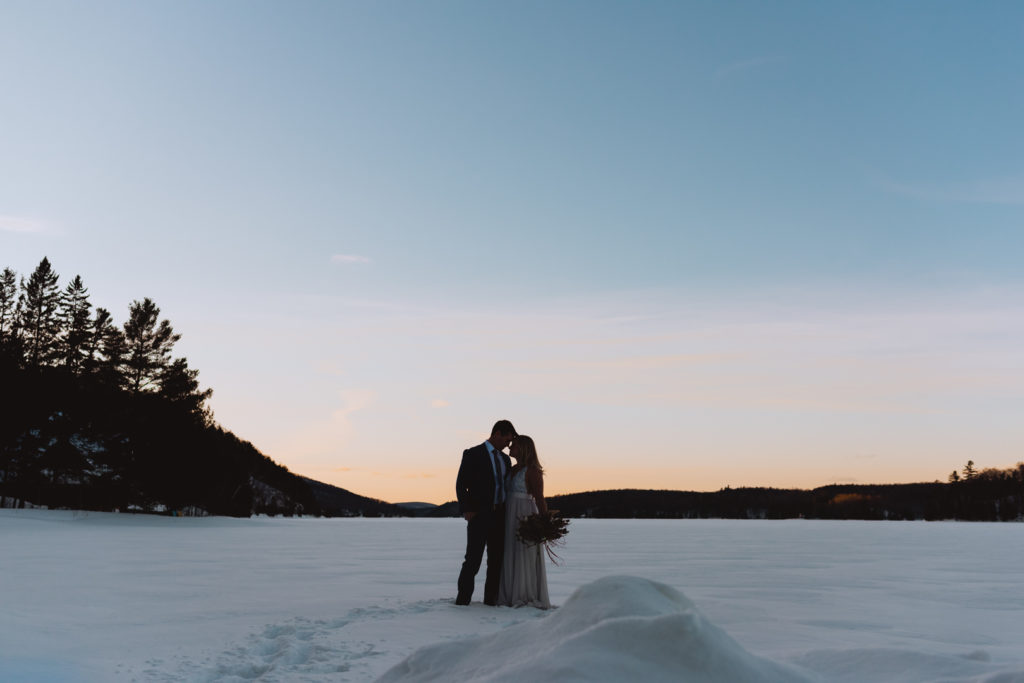 bride and groom on frozen lake at winter during sunset